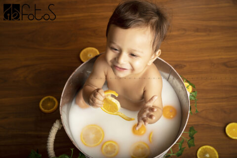 one year pre-birthday photoshoot of giggling baby boy in milk bath theme, with slice of Nagpur oranges in Nagpur.