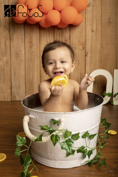 one year pre-birthday photoshoot of happy baby boy in milk bath theme, with slice of Nagpur oranges in Nagpur.